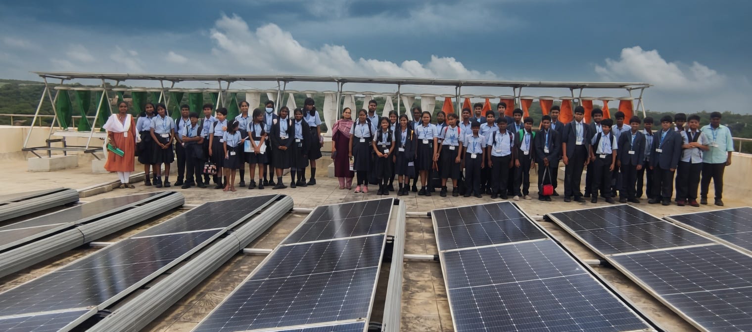 A student cohort standing among rooftop solar panels and wind turbines